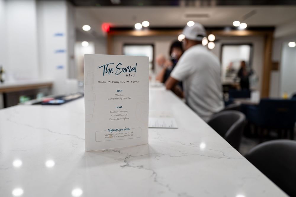 The Social menu card displayed on a white marble counter inside a modern restaurant with guests in background.