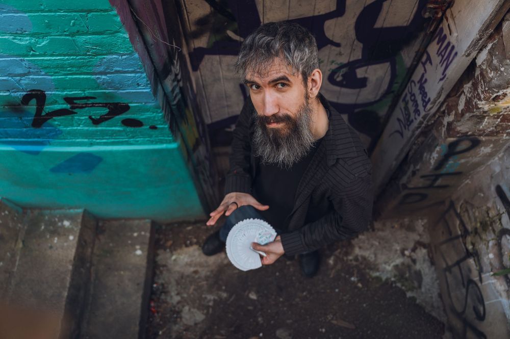 Bearded man holding playing cards in graffiti-covered urban alley, shot from above.