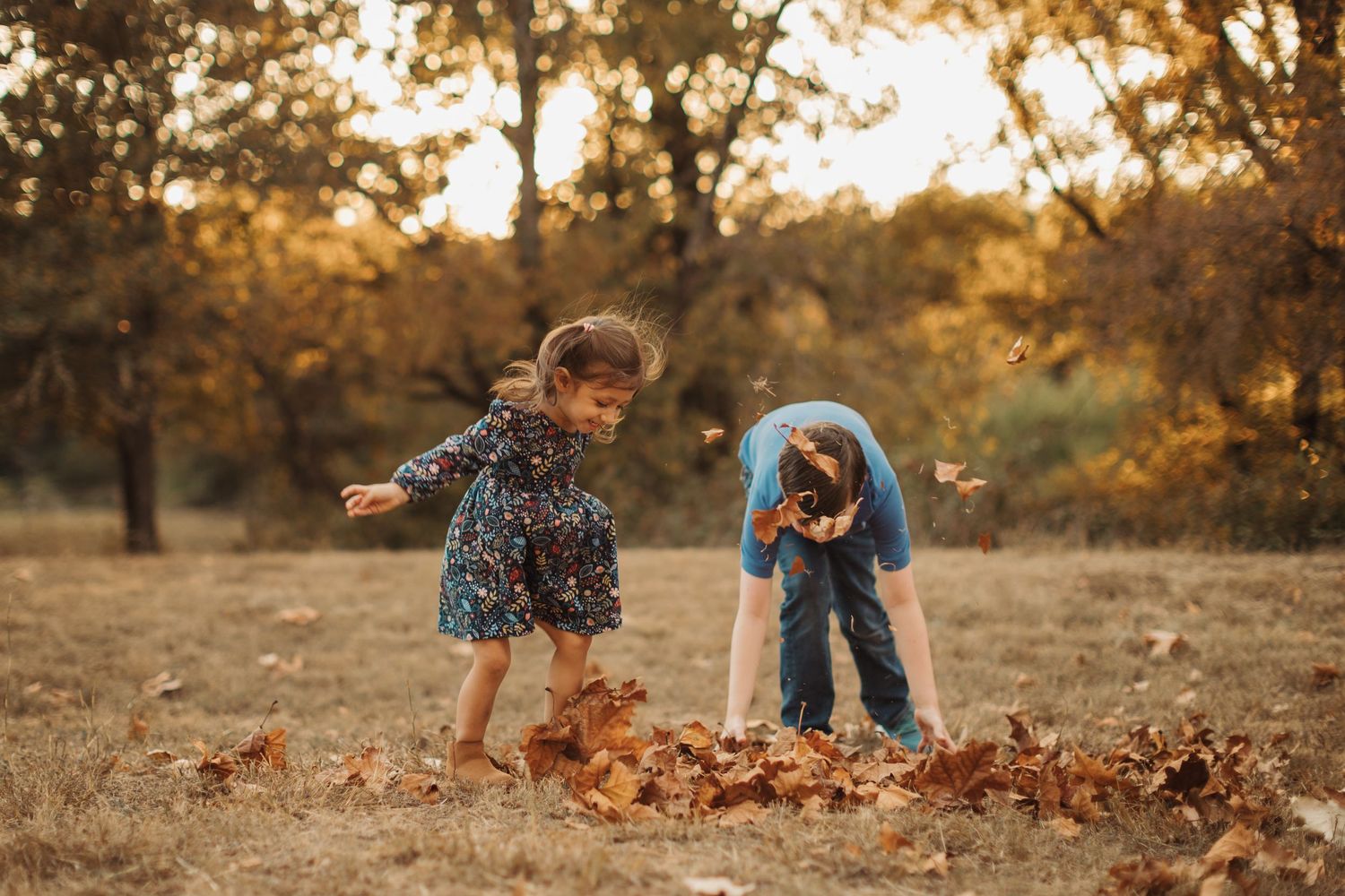 Playful autumn photoshoot with children playing with fallen leaves in a rustic outdoor setting.