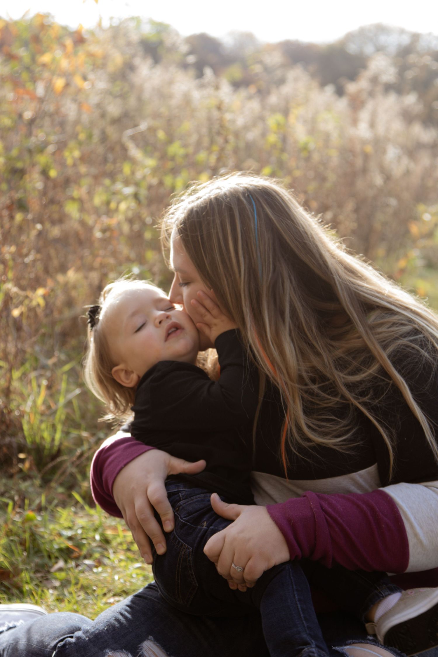 Mother and child share tender moment outdoors in autumn sunlight.
