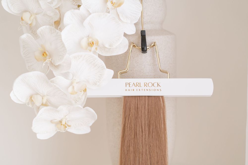 Hair extension sample displayed with white orchids and measurement tool.