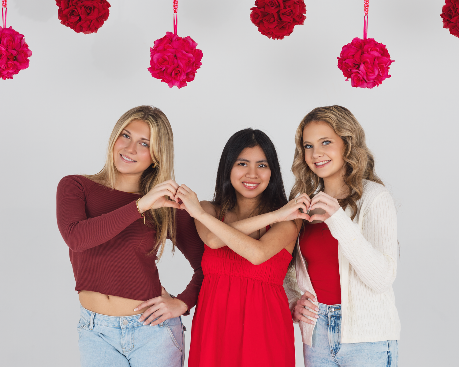 Three TFP model team members pose together against a white background with hanging pink and red pom pom decorations.