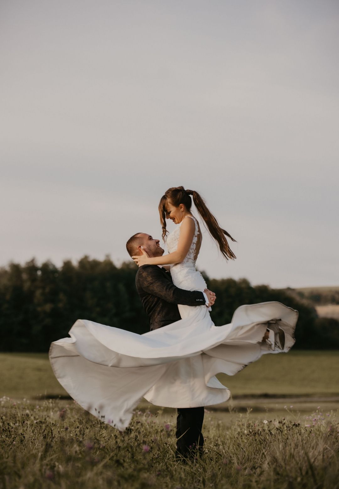 Romantic outdoor wedding photo with dress flowing in a rustic field at sunset.