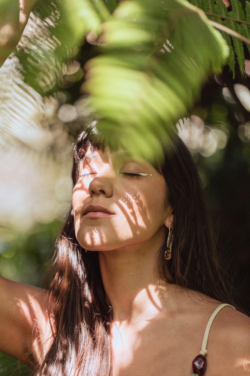 Dappled sunlight through leaves creates a dreamy pattern of shadows across a serene portrait in nature.