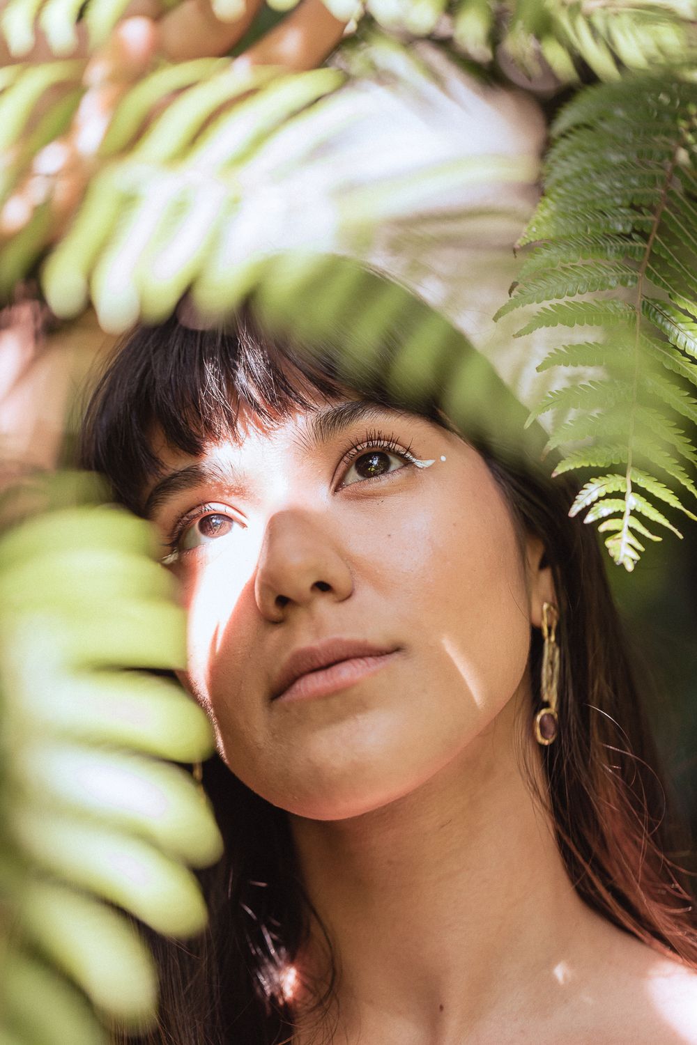 Artistic portrait framed by green fern leaves with soft natural lighting creating a dreamy atmosphere.