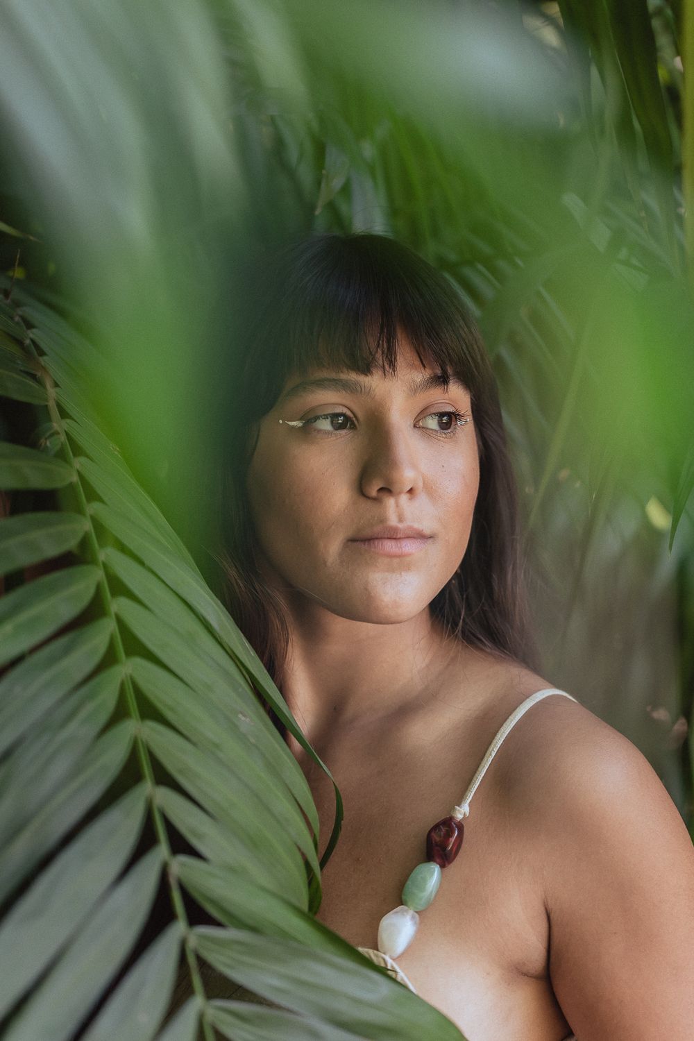 Portrait photo of person with dark hair surrounded by tropical palm leaves in soft natural lighting.