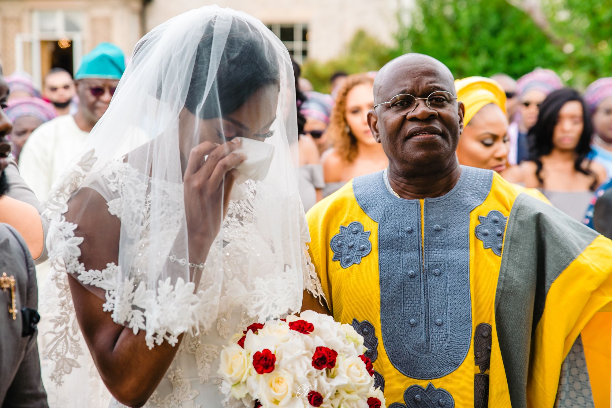 A bride holding a red and white bouquet shares a joyful moment with a person in vibrant yellow traditional attire.