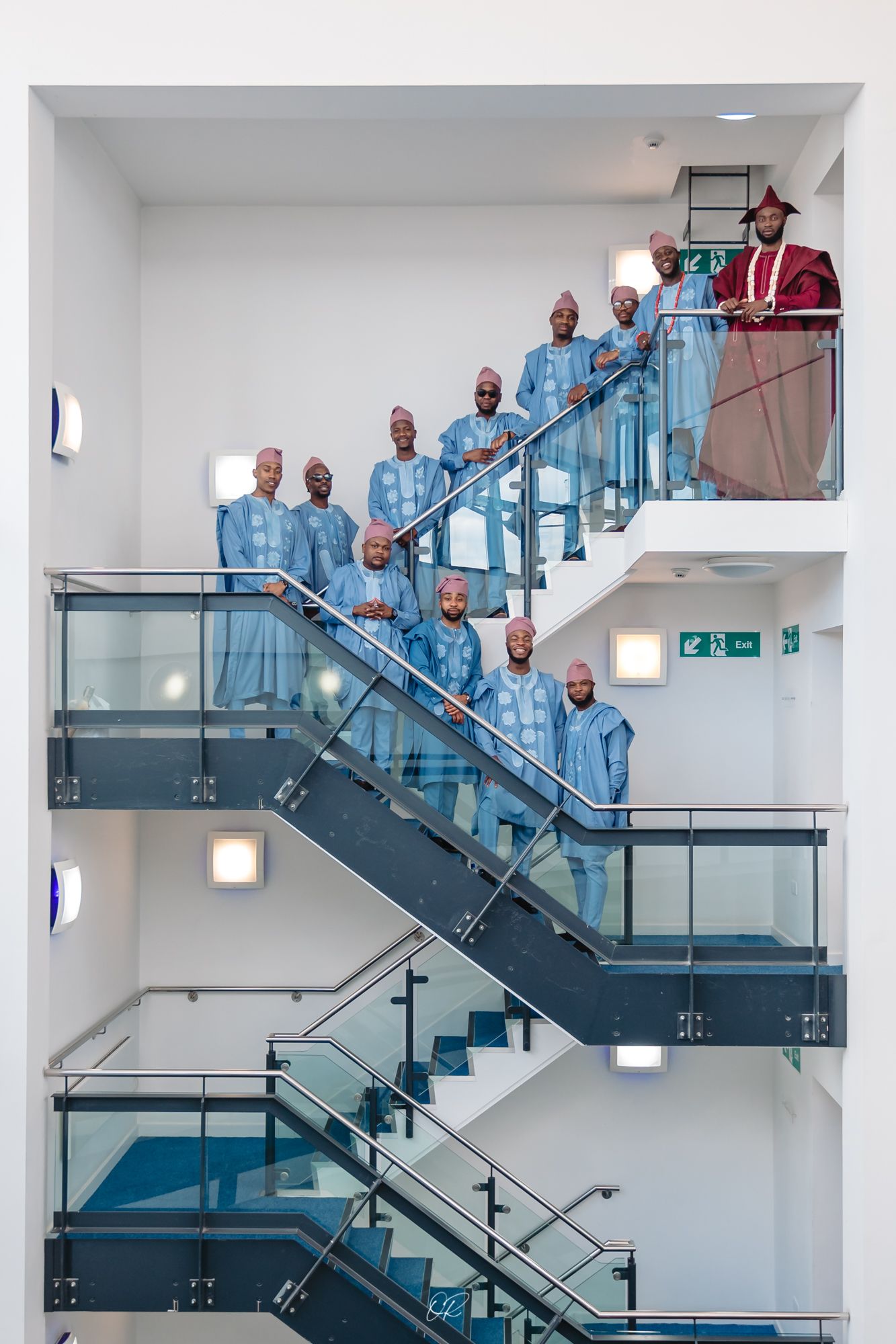 A group in matching light blue attire poses on modern glass and steel stairs in a bright interior.