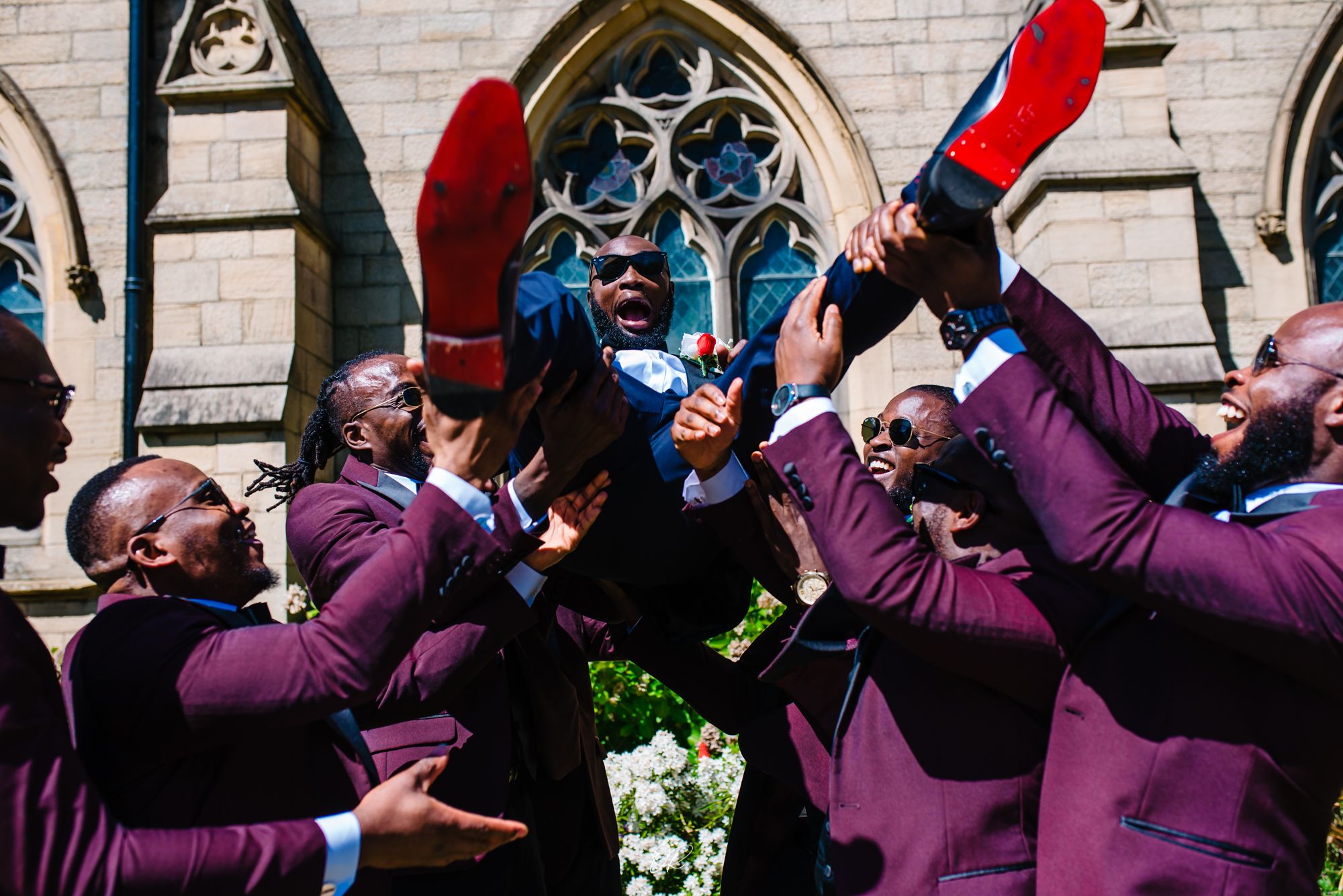 Groomsmen in purple suits celebrate joyfully outside a church with gothic architecture.