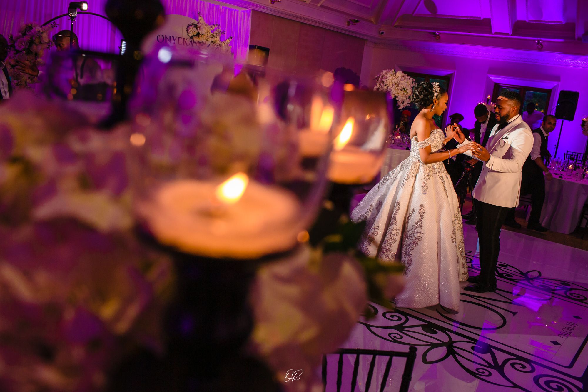 A romantic ballroom dance scene illuminated by purple lighting with candlelit tables in the foreground.