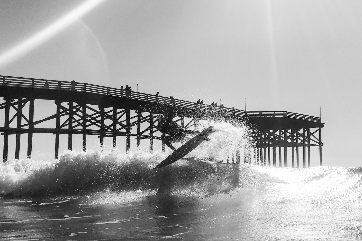Black and white San Diego surf photography of a surfer catching a wave by Crystal Pier in Pacific Beach.