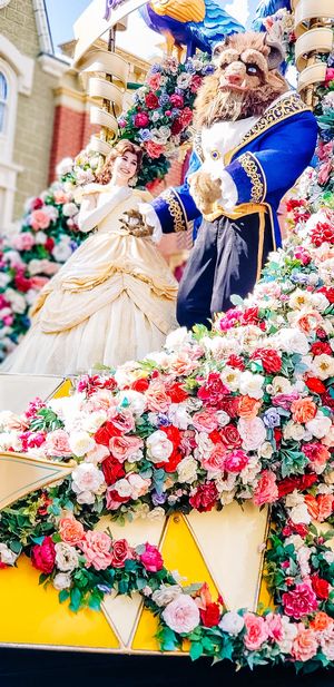 Elegant ballgowns and ornate floral decorations with pink and red roses create a romantic display at a themed event.