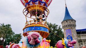 Colorful carnival float with pink decorations passes by Cinderella Castle during Disney theme park parade.
