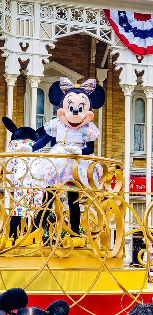 Mickey Mouse waves from a golden and red parade float at Disney park decorated with patriotic bunting and ribbons.