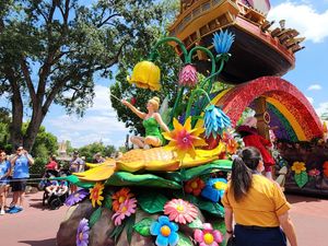Colorful Disney festival parade float adorned with vibrant flowers and characters glides through a sunny theme park.