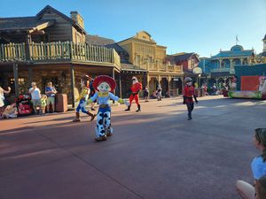 Characters and visitors stroll through a western-themed street with wooden storefronts at Magic Kingdom theme park.