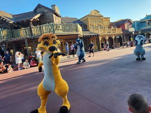 Yellow mascot characters dance and interact with guests on Main Street at Disney theme park.