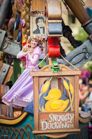 Princess in pink and purple dress poses next to wooden 'Snuggly Duckling' sign with yellow duck artwork at Disney theme park.