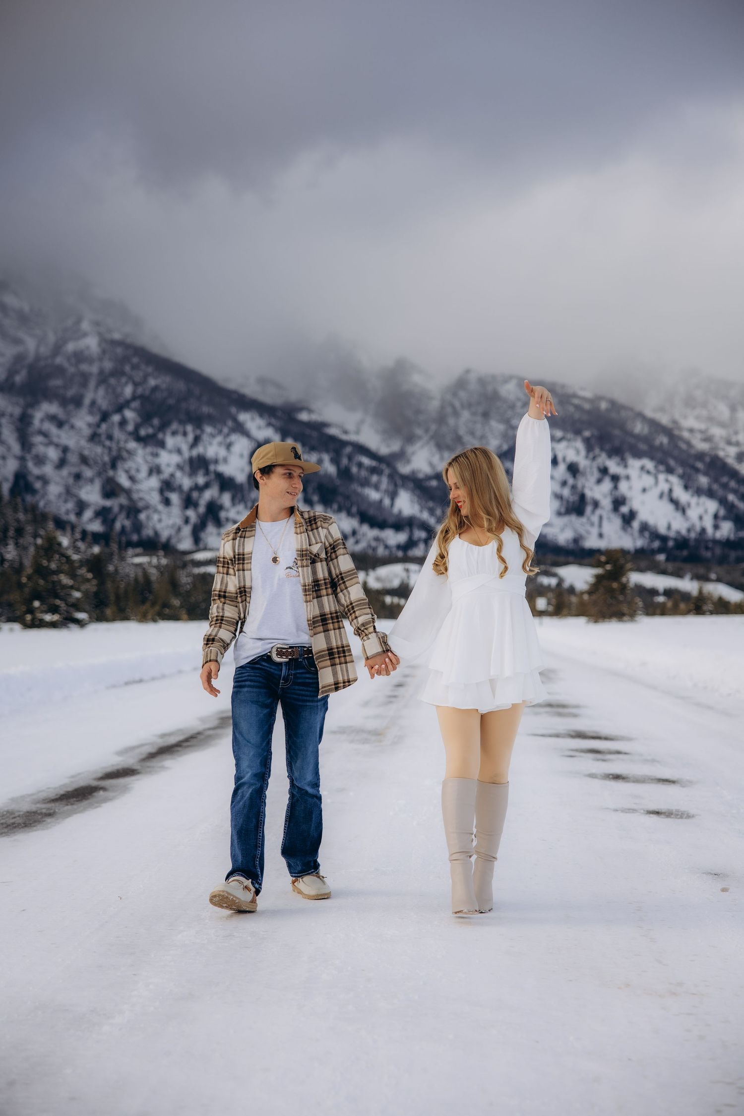 Couple holding hands while walking on snowy path with majestic snow-capped mountains in background during winter.