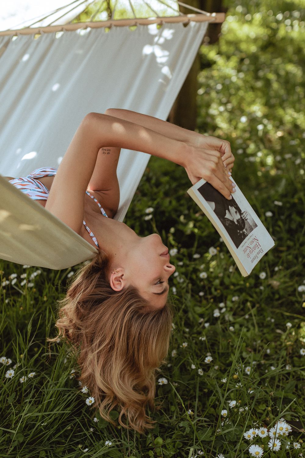 A relaxed moment reading a book while lounging in a hammock surrounded by white flowers on a sunny day.