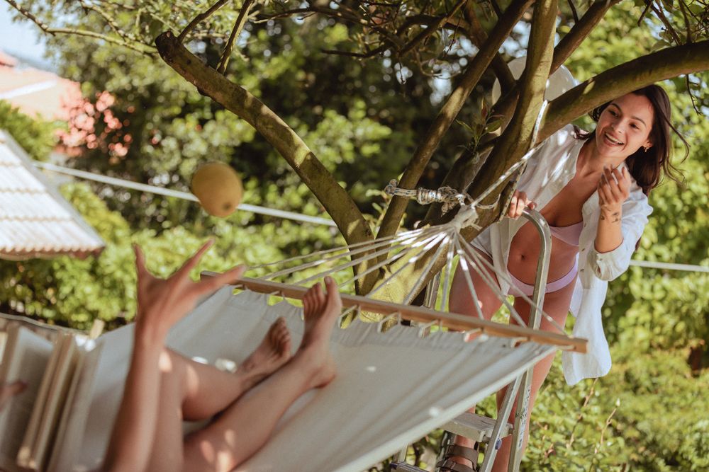 Someone relaxes in a white hammock on a sunny summer day in a lush green garden setting.