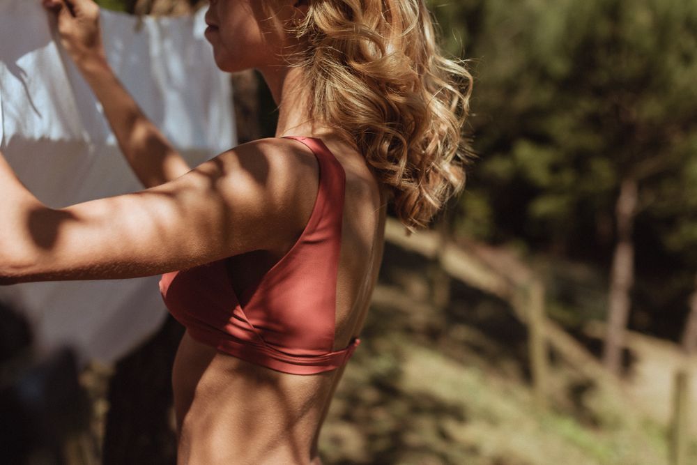 Athletic woman in pink sports bra stretches outdoors in warm sunlight during workout session.