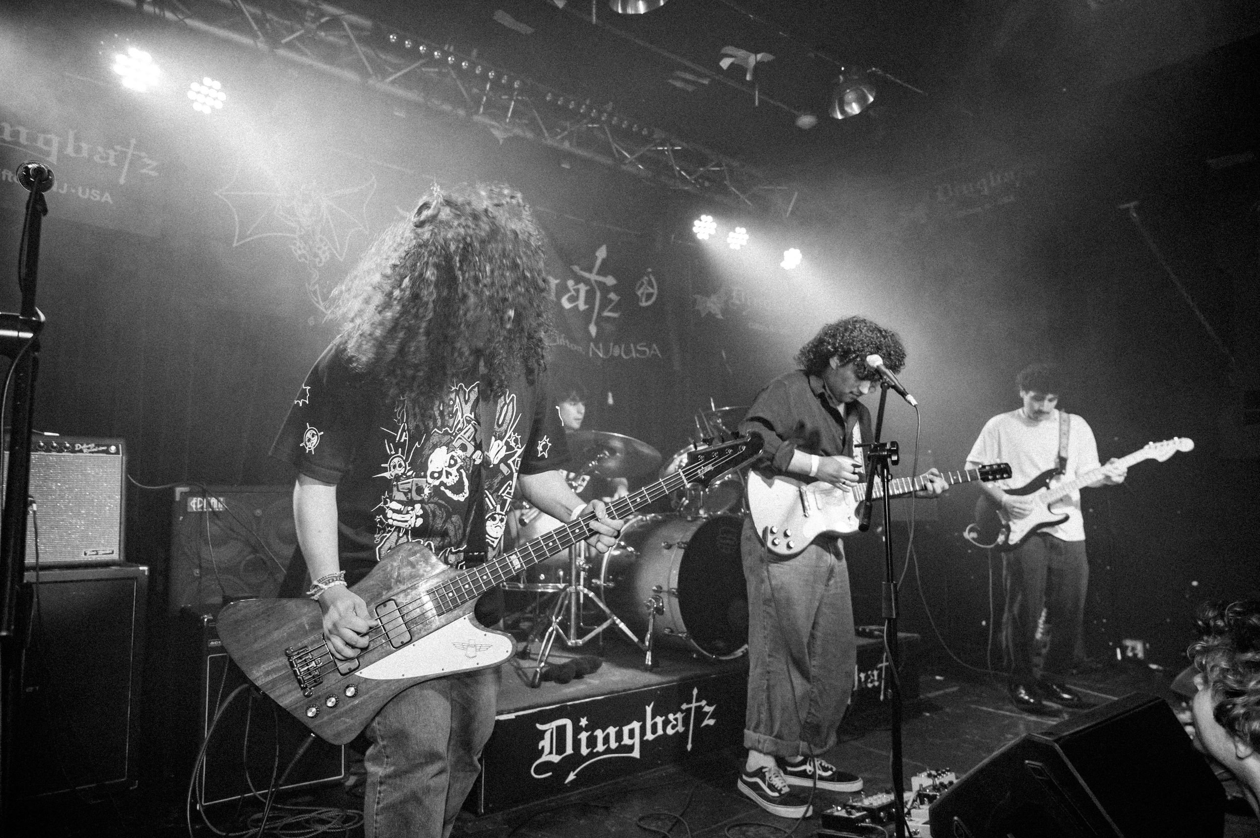 Black and white photo of a rock band performing on stage with heavy lighting effects at a live music venue.