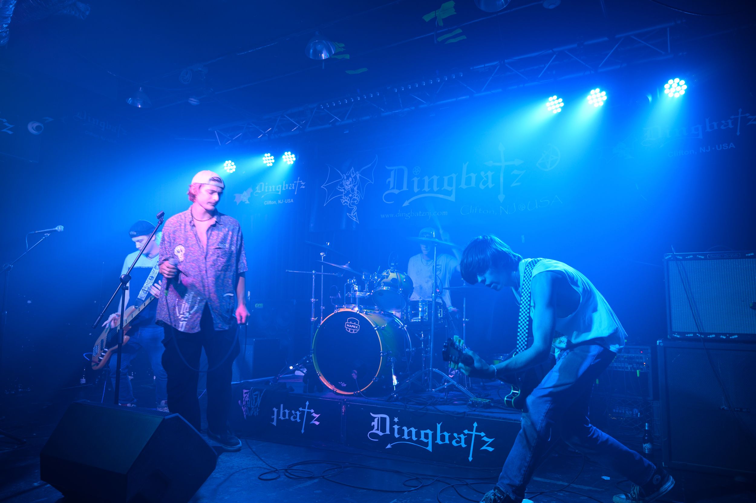 A rock band performs on stage with blue spotlights and fog effects during an energetic concert performance.