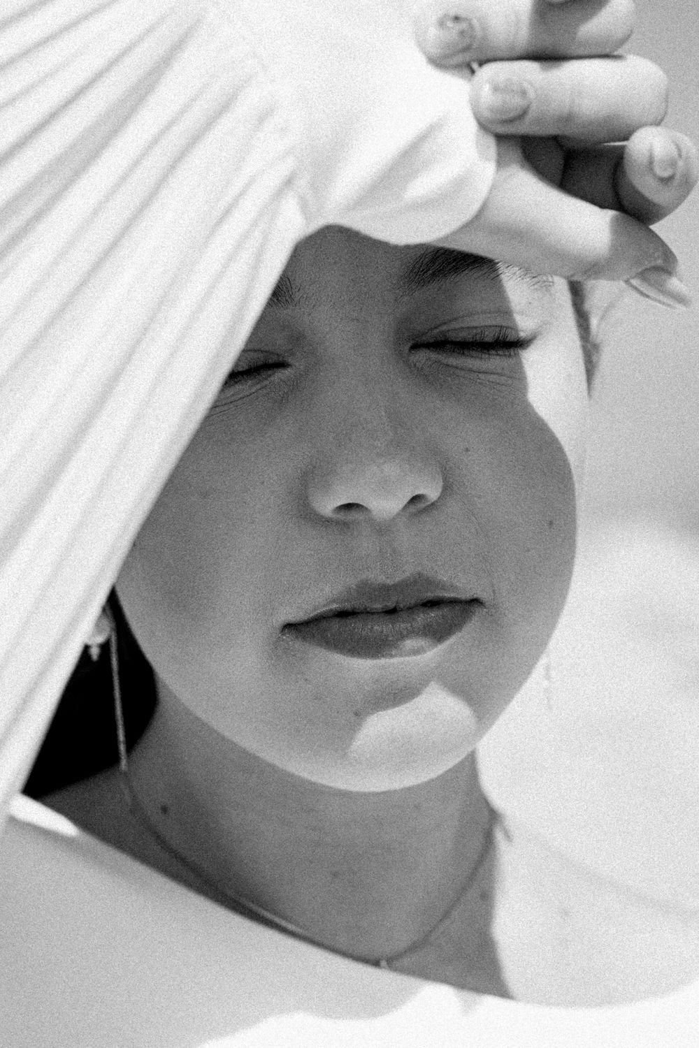 Black and white portrait of an elegant individual wearing white fabric in a serene, contemplative pose.