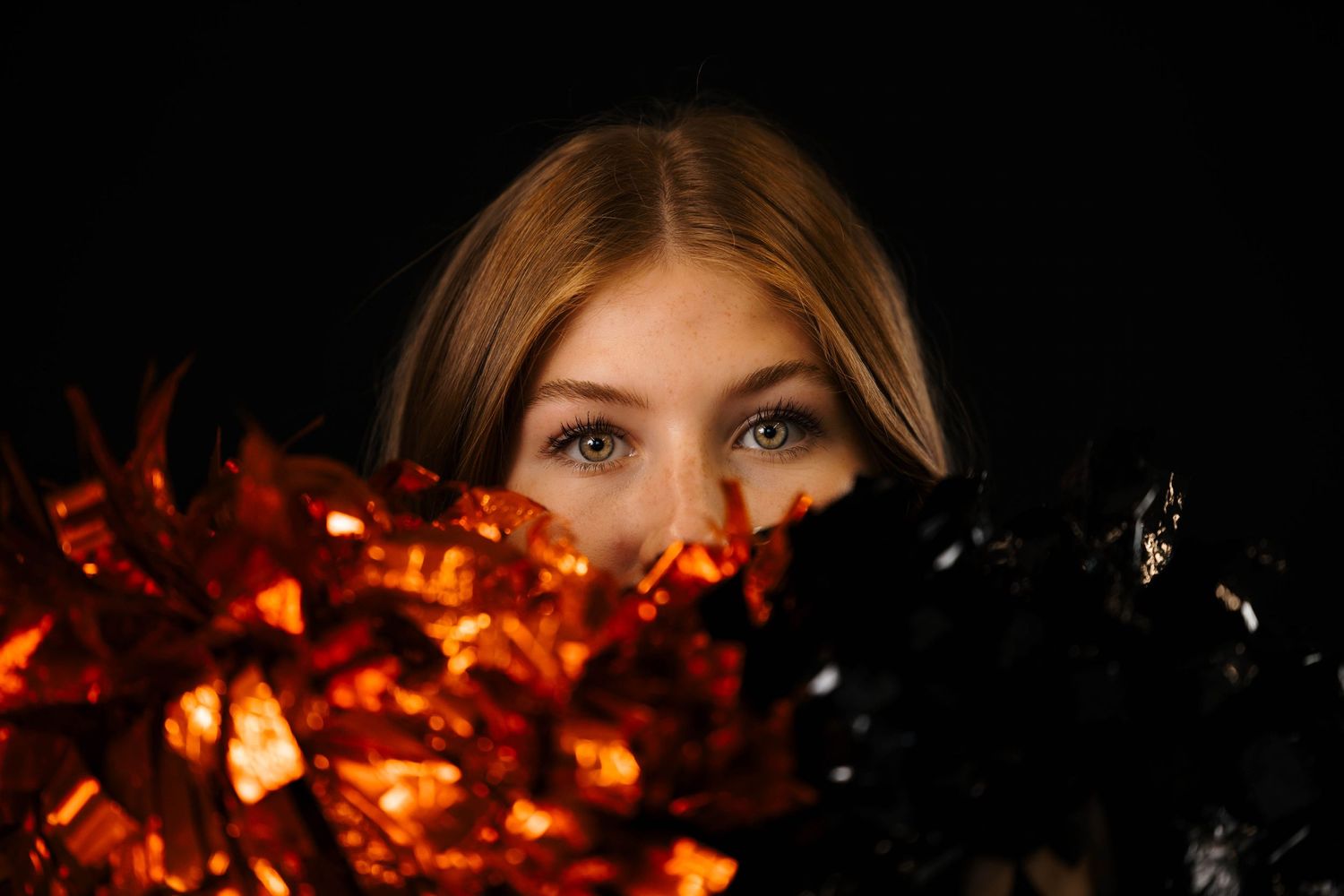 Close up of eyes peeking above orange autumn leaves and black feathers against dark background.