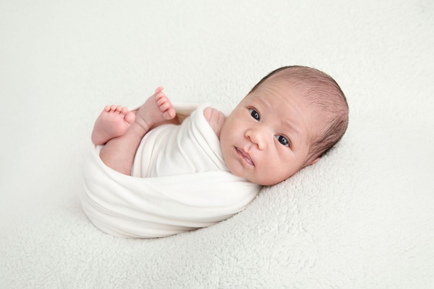 Sleeping infant wrapped in brown knit blanket resting in vintage wooden chair.