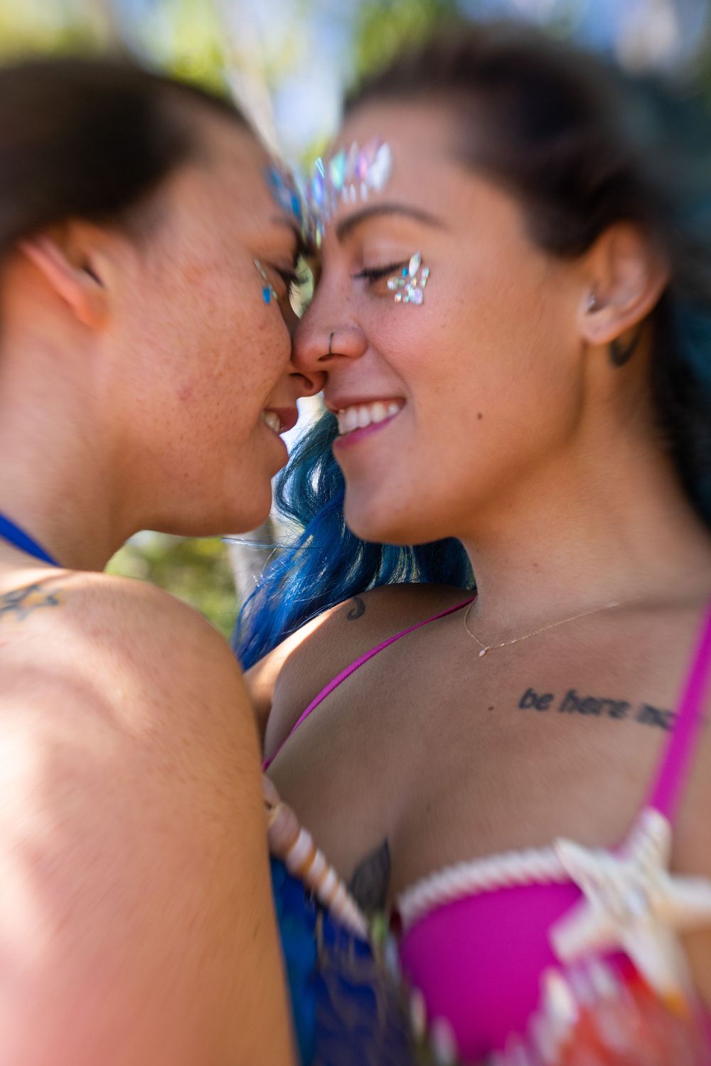 Two people with glitter makeup share a close intimate moment at a festival or celebration.