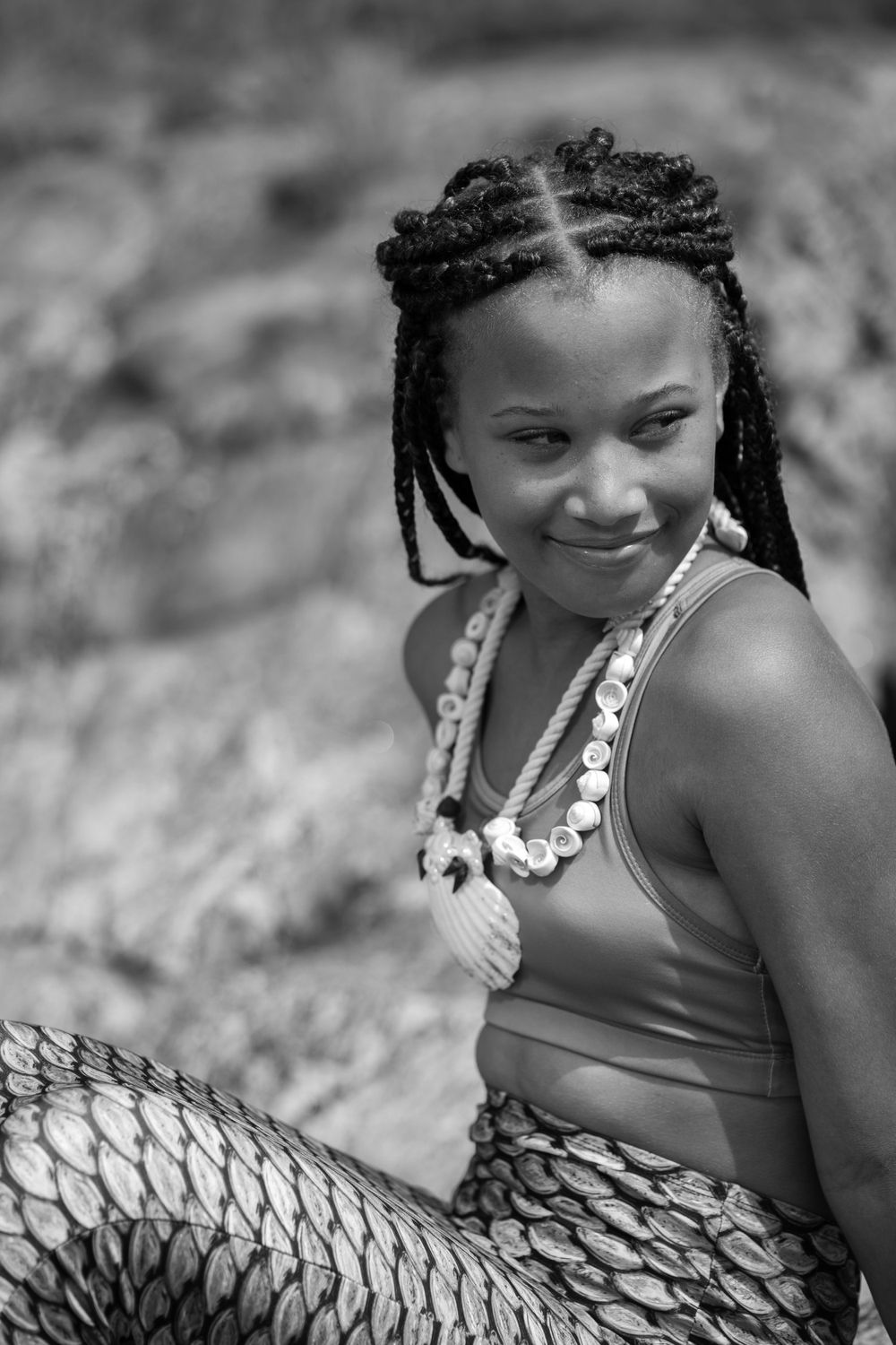 Portrait of someone with braided hair wearing shell necklaces and swimwear at the beach.