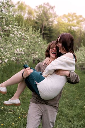 A playful moment captured as a couple laughs together in a flowering spring meadow.