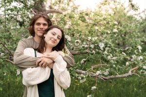Couple shares tender moments beneath flowering spring trees in a dreamy outdoor setting.