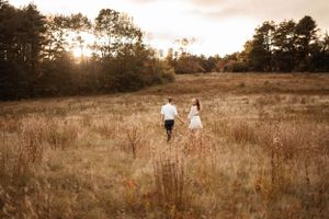 Couple walks hand in hand through a sun-drenched autumn meadow at sunset.