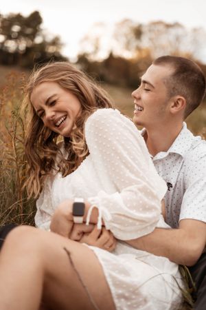 Playful couple laughing together while lying in golden autumn field.