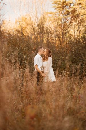 Couple shares intimate moments in tall autumn grass during golden hour photoshoot.