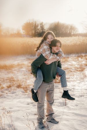 A playful piggyback ride sequence captured in a snowy field during golden hour.