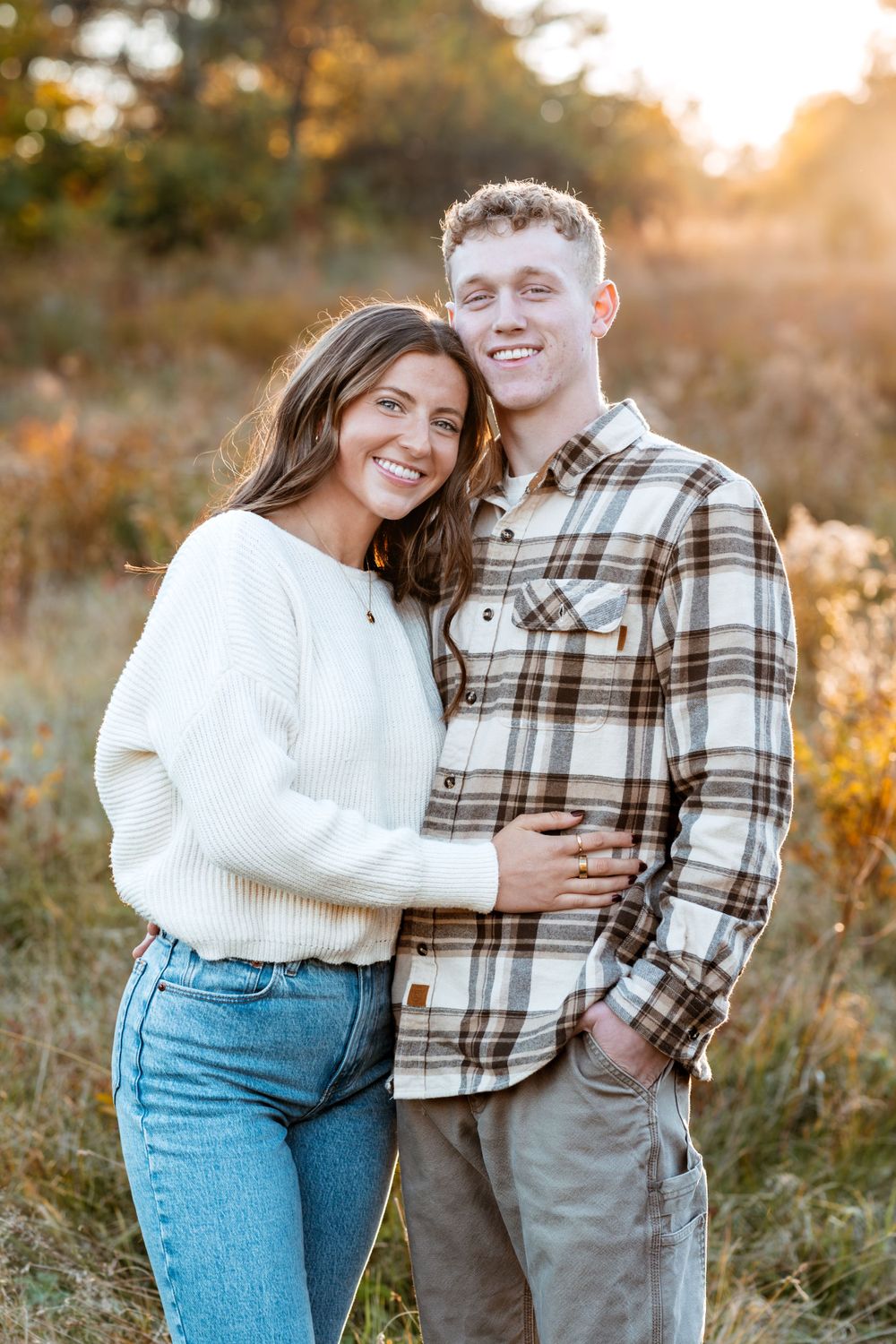Couple in casual fall outfits embracing outdoors during golden hour sunset.