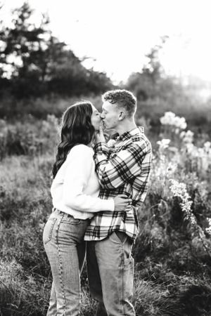 A romantic black and white portrait of a couple embracing in a sunlit field with wildflowers.