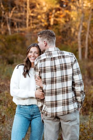Couple in white sweater and plaid shirt sharing intimate moments against fall foliage.