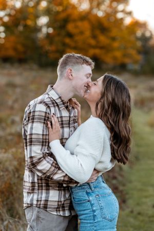 Romantic couple sharing tender kiss in autumn field wearing coordinated casual outfits.