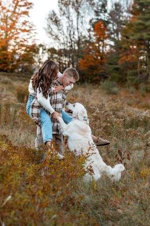 White dog playing with couple in autumn field during sunset photoshoot.