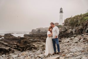 A romantic coastal portrait with a lighthouse perched on rocky cliffs in the background.