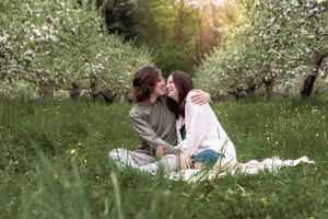 A couple shares a romantic moment on a blanket in a blooming spring orchard.