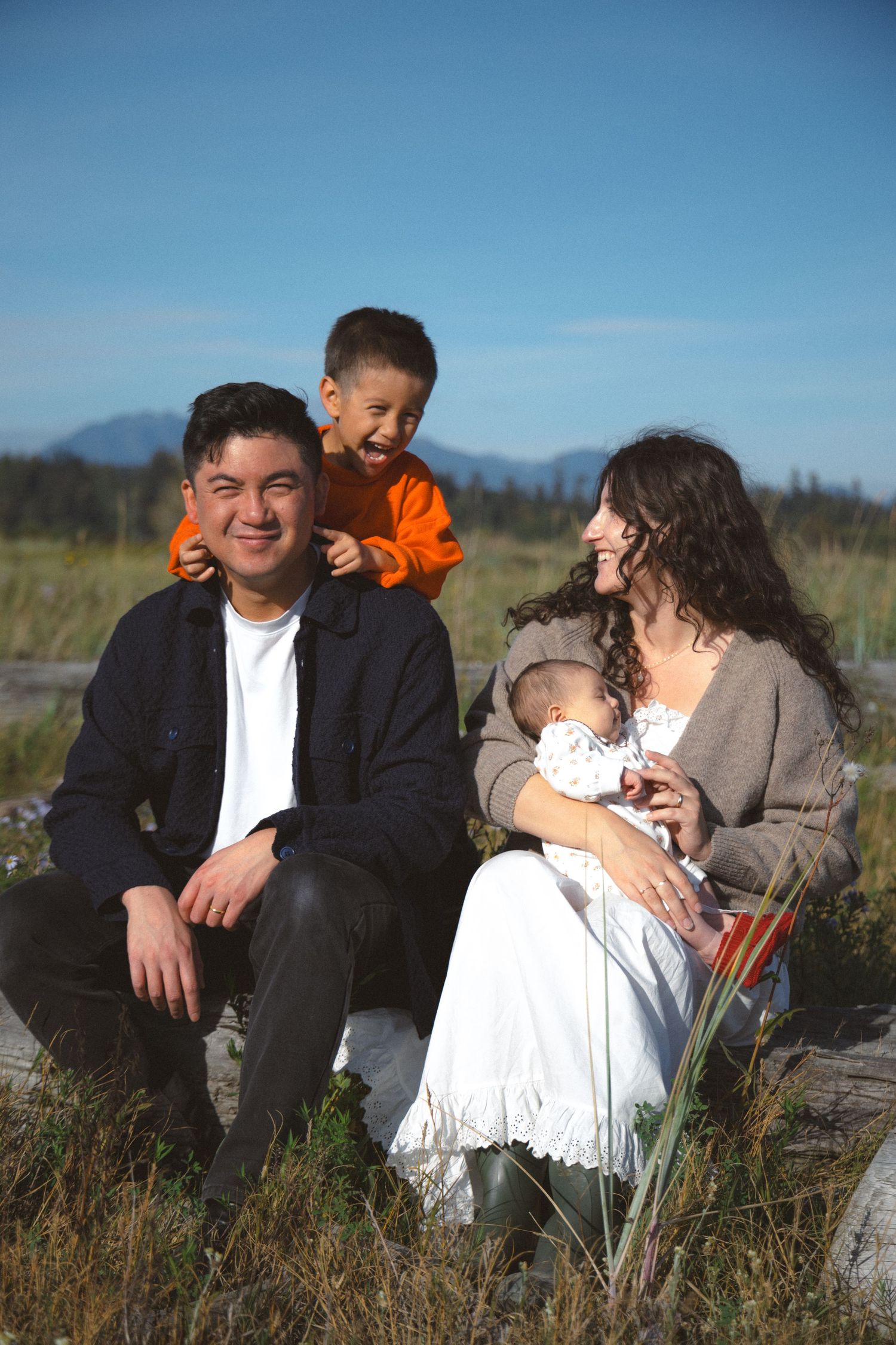 Candid family portrait of a family of four outside at Iona beach with blue skies during a vancouver family photoshoot.