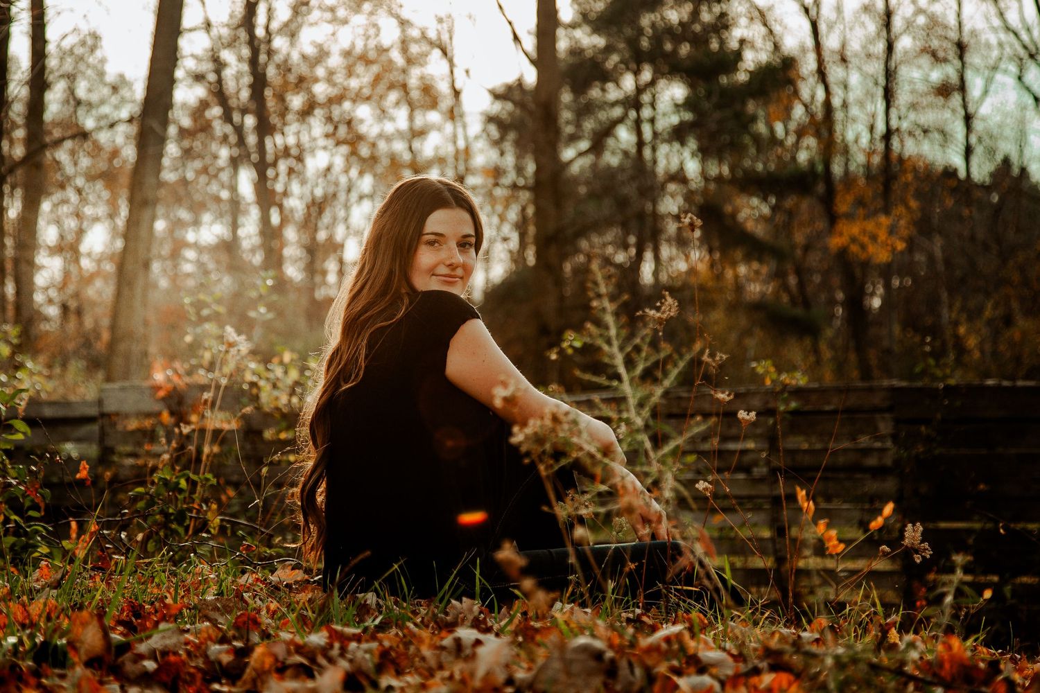 Portrait of a woman sitting among autumn leaves in a misty forest setting.
