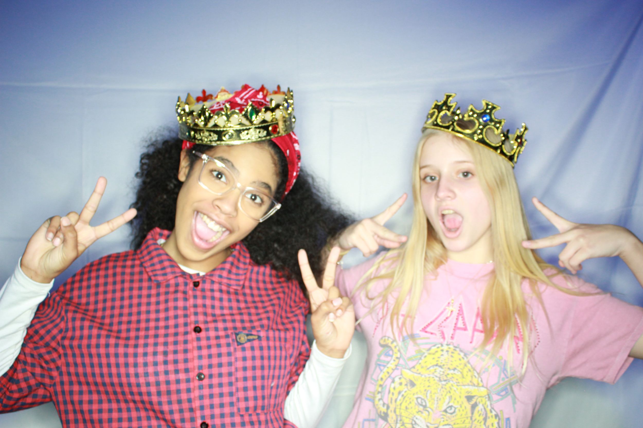 Two people wearing flower crowns making peace signs and silly expressions in a photo booth style picture.