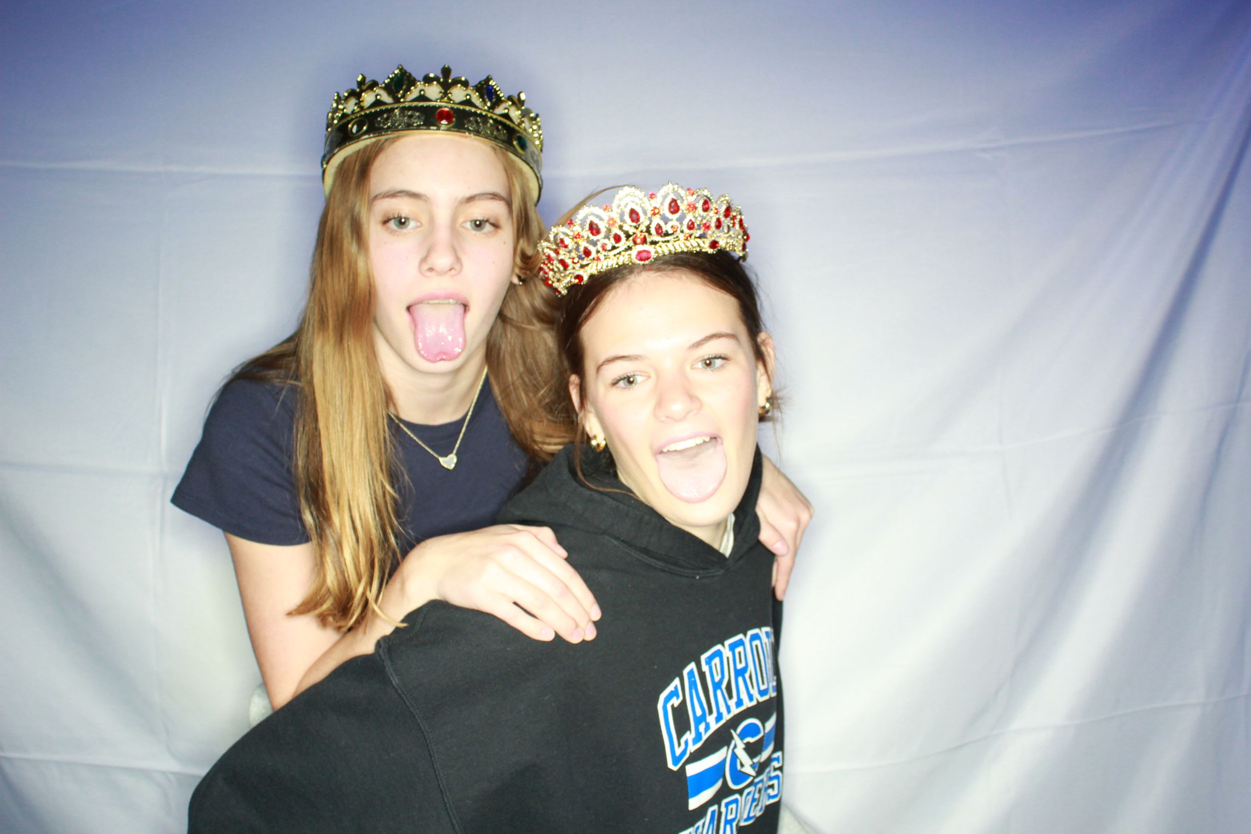 Two friends pose together playfully against a light colored backdrop in a casual photo booth style shot.